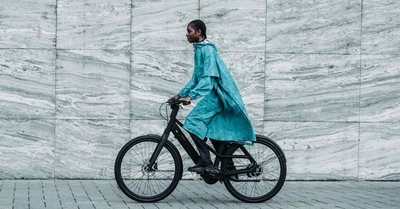 De MAIUM x Van Gogh Museum collectie, vrouw op fiets in regenjas met Van Goghs Amandelbloesem